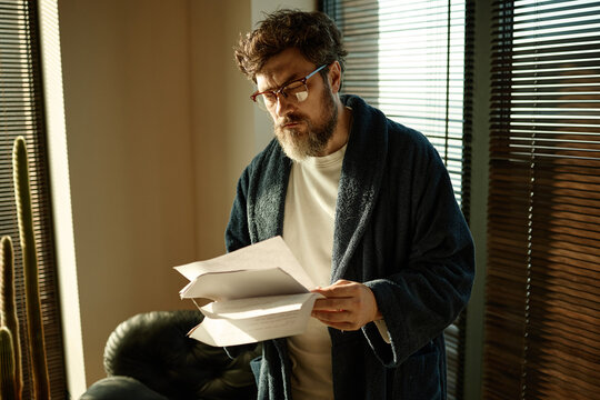 Middle aged Caucasian man reading paperwork at home, reviewing novel, checking spelling
