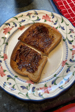 Cooked toast halves on a patterned plate, spread generously with vegemite