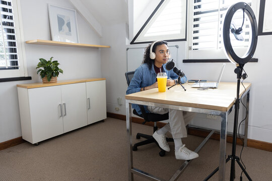 Non-binary creator sitting loft office speaking into mic, denim jacket, using laptop, copy space