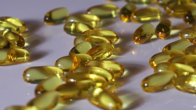 Golden omega 3 fish oil capsules scattered on a white reflective surface in close up view. Healthy dietary supplement and wellness concept.