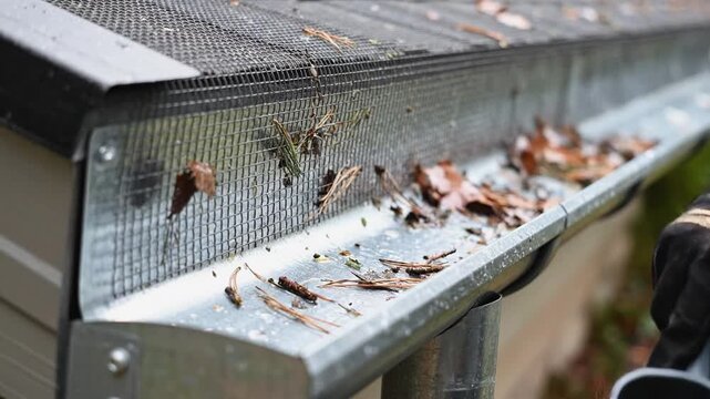 Individual cleaning debris from gutter using scoop tool, showcasing progression of action