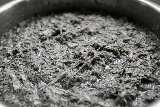 Close up macro texture of wet gray shredded paper pulp mush inside a round metal recycling vat