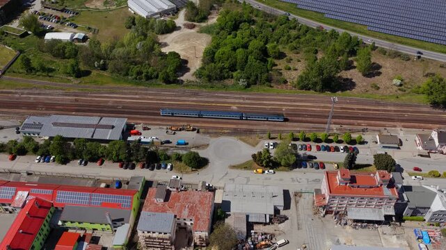 Aerial view of industrial buildings, a railway line with a train, and parking lots surrounded by green trees in Slavkov u Brna, South Moravian Region, Czechia.