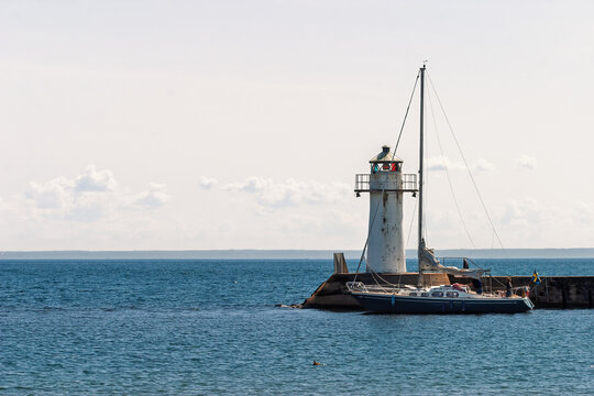 Lighthouse on a pier with a sailboat on a calm lake a summer day