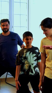 Indian family doing virabhadrasana yoga at home practicing warrior pose together indoors for healthy body and calm mind during morning routine inside a modern lavish living space
