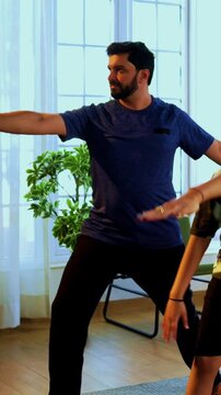 Indian family doing virabhadrasana yoga at home practicing warrior pose together indoors for healthy body and calm mind during morning routine inside a modern lavish living space