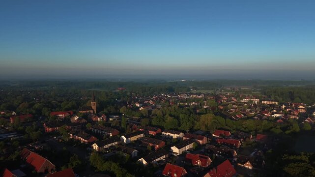 German city neighborhood with traditional orange tile roofs and historic church tower during golden hour sunrise as camera flies over residential apartment blocks. Aerial drone flyover shot.