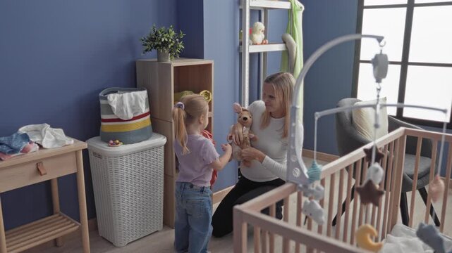 Mother kneels and accepts a stuffed kangaroo from daughter by crib in nursery building; tenderness playtime.