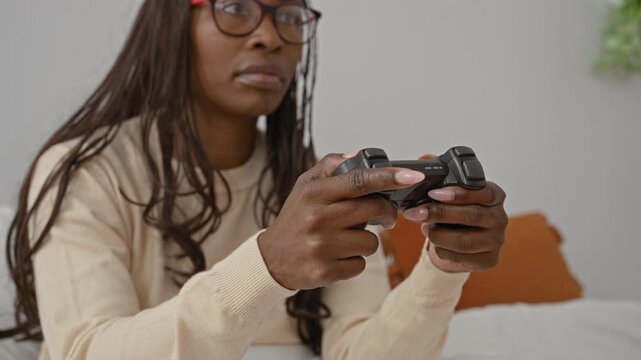 Woman gripping game controller while seated on bed in bedroom, hands visible on joystick and buttons; concentration.