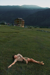 Fototapeta premium A woman lies on a grassy field outdoors, distant house and mountains in the background, conveying relaxation, leisure, and a moment of nature inspired calm.