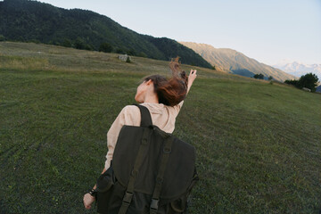 Fototapeta premium Joyful woman outdoors, backpack on shoulder, arms lifted, sunlit meadow with distant mountains, carefree lifestyle, natural colors, gentle breeze, exploring moment today