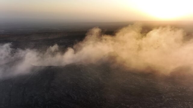 Aerial view of thick white smoke rising from dark volcanic rock in the Danakil Desert during sunset Dalol, Afar, Ethiopia.