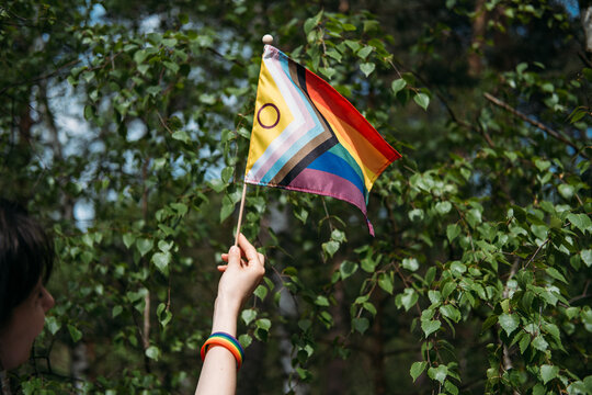 Hand holds inclusive pride flag against foliage. lgbtq diversity and inclusion, corporate pride support, lgbtq friendly business.