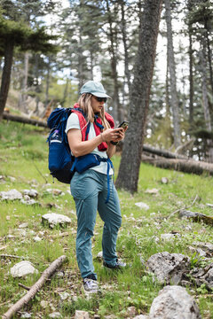 Woman is hiking in a forest. She wears a blue backpack and a cap