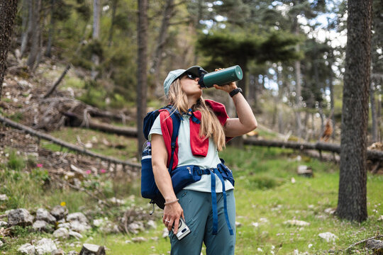 Young woman drinks from water bottle while hiking in forest