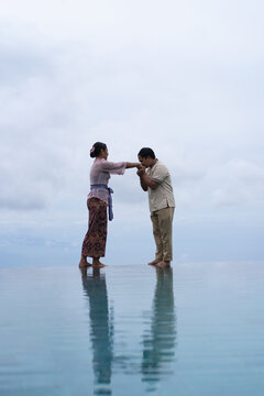 Balinese man kissing woman's hand at infinity pool, Bali