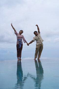 oyful Balinese couple making heart shape at infinity pool, Bali