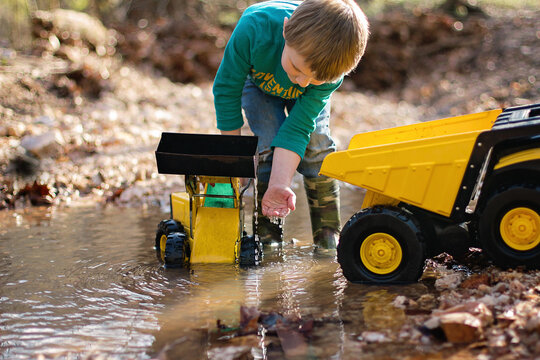 Little Boy Playing In Stream With Toy Trucks