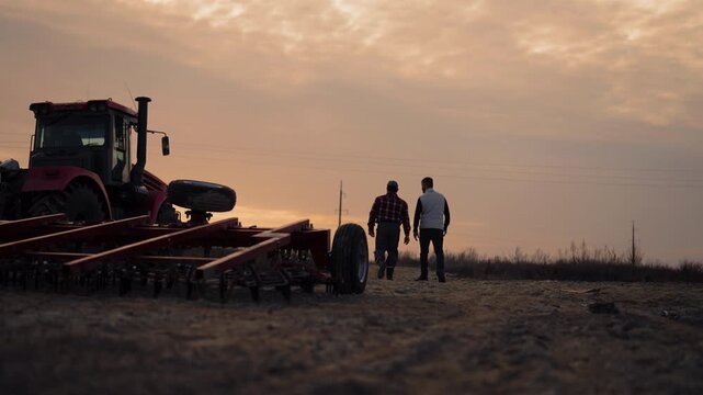 Agronomy and farming in ecological region, modern agricultural machinery. Farm workers walking near huge tractor or harvesting combine in field in sunset or sunrise, agribusiness and agriculture