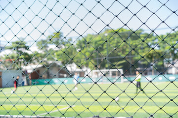 Protective netting in front of a soccer field, with blurred players and goal in the background.  sports themed scene with depth and focus. © Rijjal