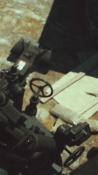 Tools and machines are scattered on a wooden workbench. A piece of paper sits on the bench. The setting shows signs of use. Light comes from a window overhead.