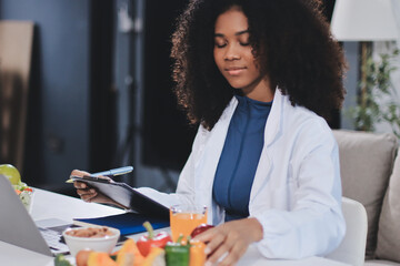 Fototapeta premium Young nutritionist showing bell peppers during an online video call consulting about healthy eating, sitting at home at a table with vegetables, laptop and measuring tape