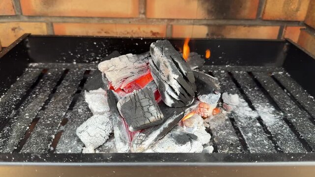 A pile of black charcoal briquettes newly lit and burning inside a metal grill with hot glowing red embers, sparks and intense smoke for backyard bbq.
