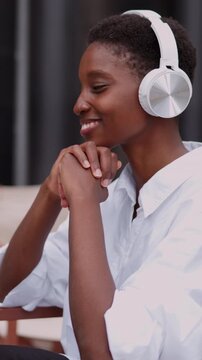 focused young Black woman in headphones participating in online English learning class. Seated at outdoor caf&eacute;, female interacts with her laptop computer, absorbed in lesson. educational atmosphere
