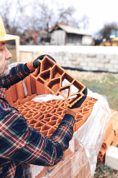 Bricklayer mason holding a regular brick outdoors on a construction site.