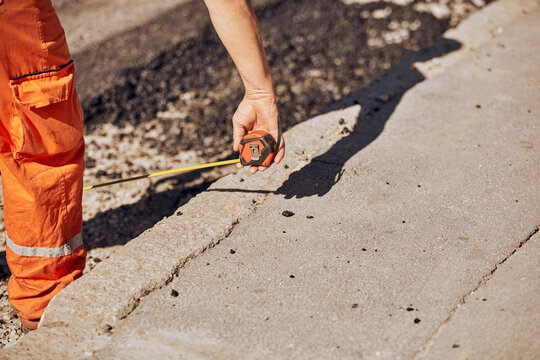 Construction worker using tape measure to measure dimensions of the street during reconstruction.