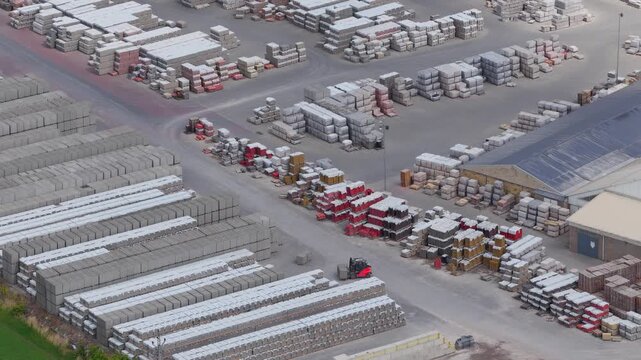 Aerial view of an industrial storage yard with organized stacks of building materials and a forklift moving between pallets in Otnice, South Moravian Region, Czechia.