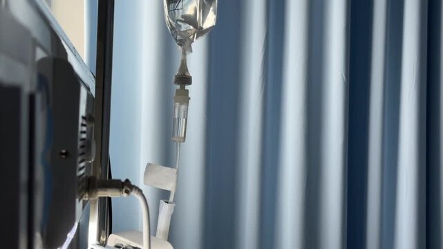 Medical IV drip chamber with liquid dropping, hospital background with blue curtains and cinematic lighting.