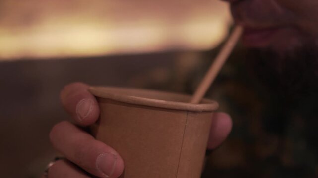 Primer plano de hombre bebiendo en vaso de papel biodegradable con pajita de cart&oacute;n reciclable. Close up of man drinking from biodegradable paper cup with recyclable cardboard straw.