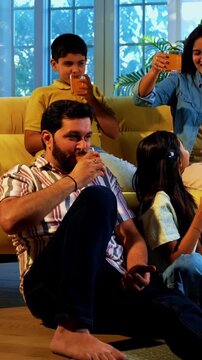 Indian family together drinks cold drink in glass as mother serves refreshing beverages to husband and kids while everyone enjoys happy bonding time indoors in modern lavish home
