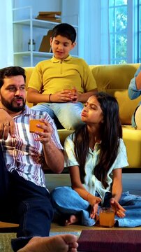 Indian family together drinks cold drink in glass as mother serves refreshing beverages to husband and kids while everyone enjoys happy bonding time indoors in modern lavish home