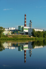Fototapeta premium An industrial factory on the riverbank. The factory's reflection in the water. Smoke from the chimney of a furniture factory