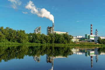 Obraz premium An industrial factory on the riverbank. The factory's reflection in the water. Smoke from the chimney of a furniture factory