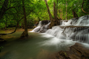 A turquoise waterfall cascades down in layers in the middle of the forest. © Pongsorn