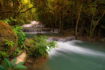 A turquoise waterfall cascades down in layers in the middle of the forest. © Pongsorn