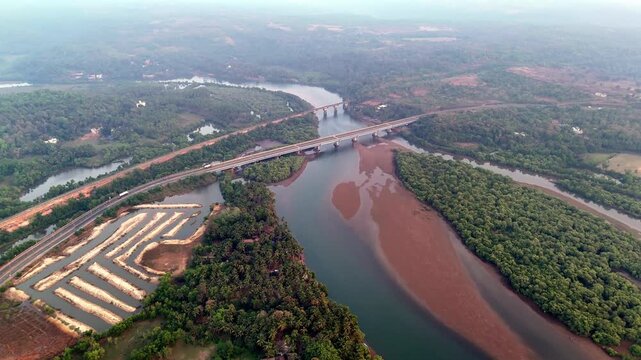 Cinematic aerial view of Talpona Bridge spanning across a winding river surrounded by dense mangrove forests, with exposed sandbanks creating striking natural patterns through the waterway.