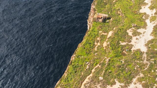 Drone shot of the high limestone Dingli Cliffs, revealing an old military coastal building on the edge of the precipice overlooking the Mediterranean Sea, Malta