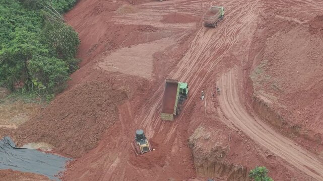 A crawler bulldozer is leveling the fill soil unloaded from a truck for road construction