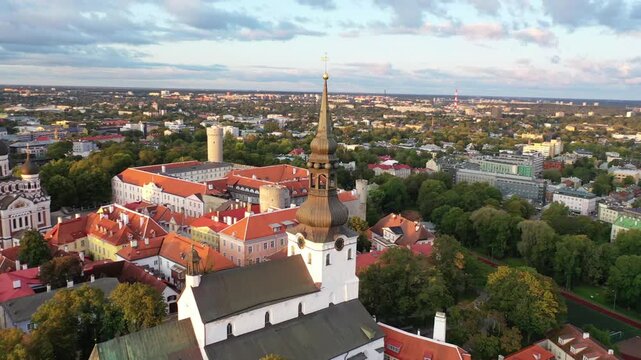 Breathtaking drone footage of Tallinn's medieval Old Town at sunset. The shot features Toompea Hill, St. Mary's Cathedral, and red-roofed buildings under a dramatic sky of pink and orange clouds.