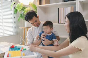 Obraz premium Happy young family playing with baby at home, parents engaging child with colorful toys and learning activities, showing love, care, early childhood development, and warm bonding moment together.