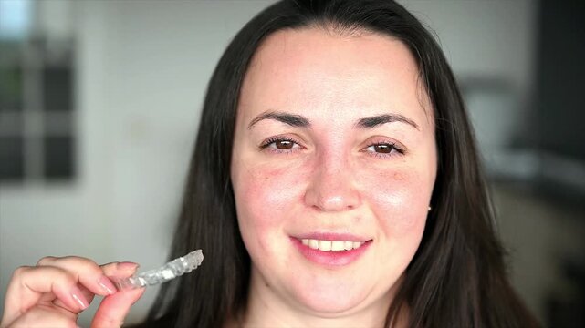 Woman holding transparent dental aligner close to camera demonstrating flexibility and clarity of material, modern invisible orthodontic appliance detail and quality