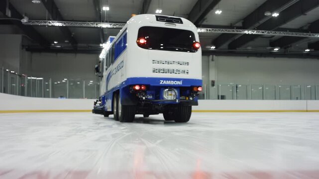 Ice resurfacing machine glides across rink, showcasing wheels and blades as it prepares smooth surface for skating, illuminated by overhead lights in indoor arena