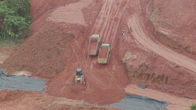 A crawler bulldozer is leveling the fill soil unloaded from a truck for road construction