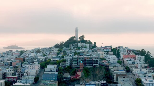 Elevated view of San Francisco's North Beach neighborhood with the iconic Coit Tower on Telegraph Hill and Alcatraz Island in the bay during a cloudy and foggy sunset