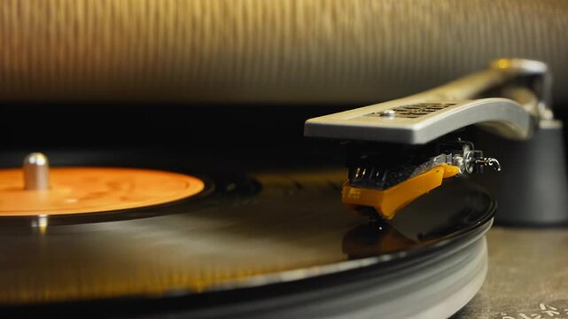 Close-up view of a turntable needle lowering onto a spinning vinyl record, capturing the moment of contact and sound initiation in a cozy indoor setting