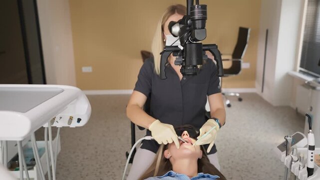 Female dentist using dental microscope during treatment of patient in clinic. Concept of modern dentistry and oral healthcare.
